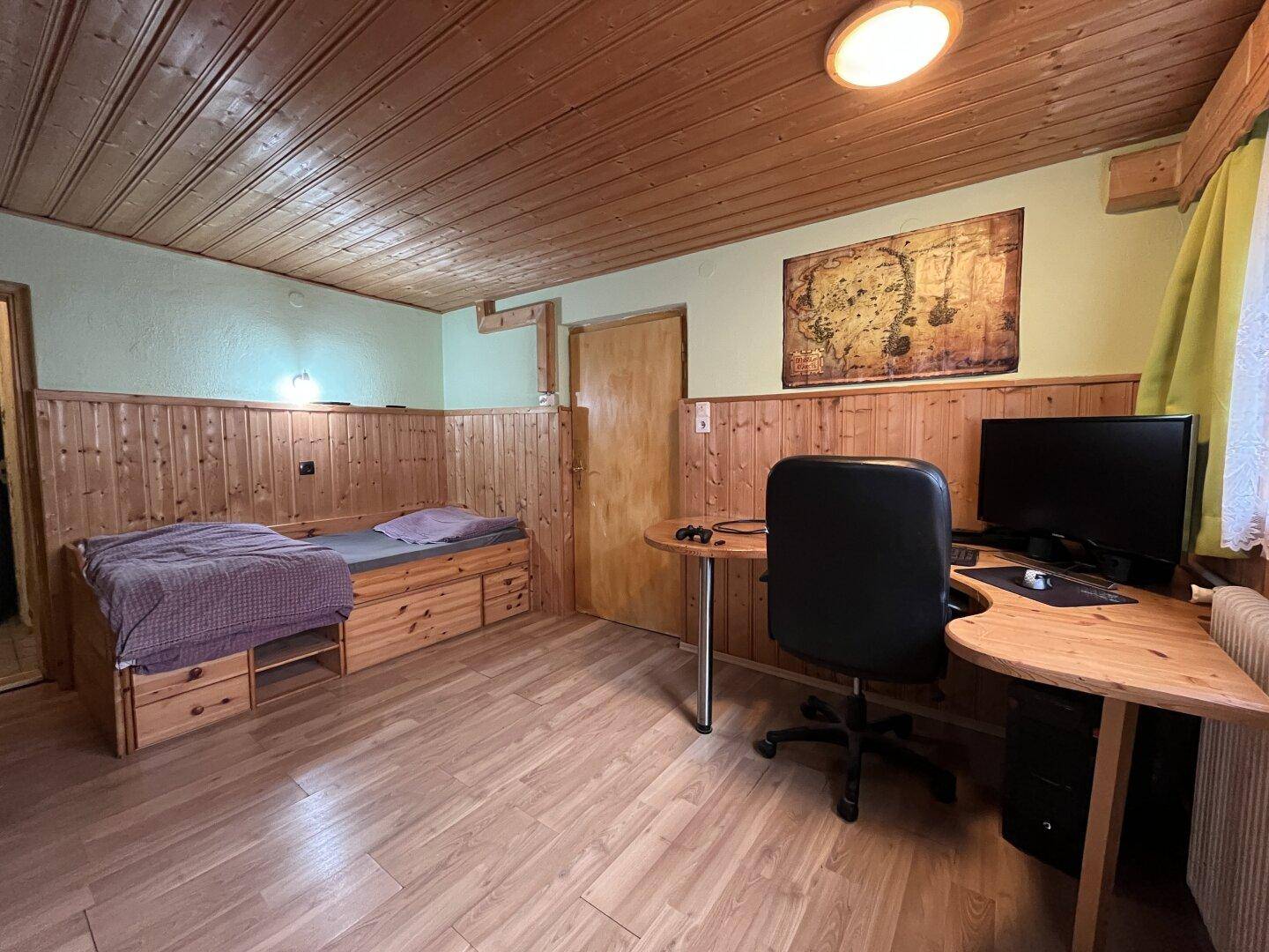 Schlafzimmer mit Holzvertäfelung, Einzelbett und Schreibtisch.