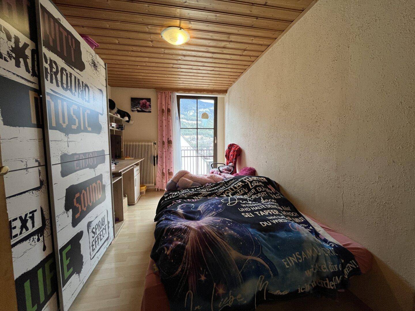 Kinderzimmer mit Einzelbett, Laminatboden und Zugang zu einem französischen Balkon.