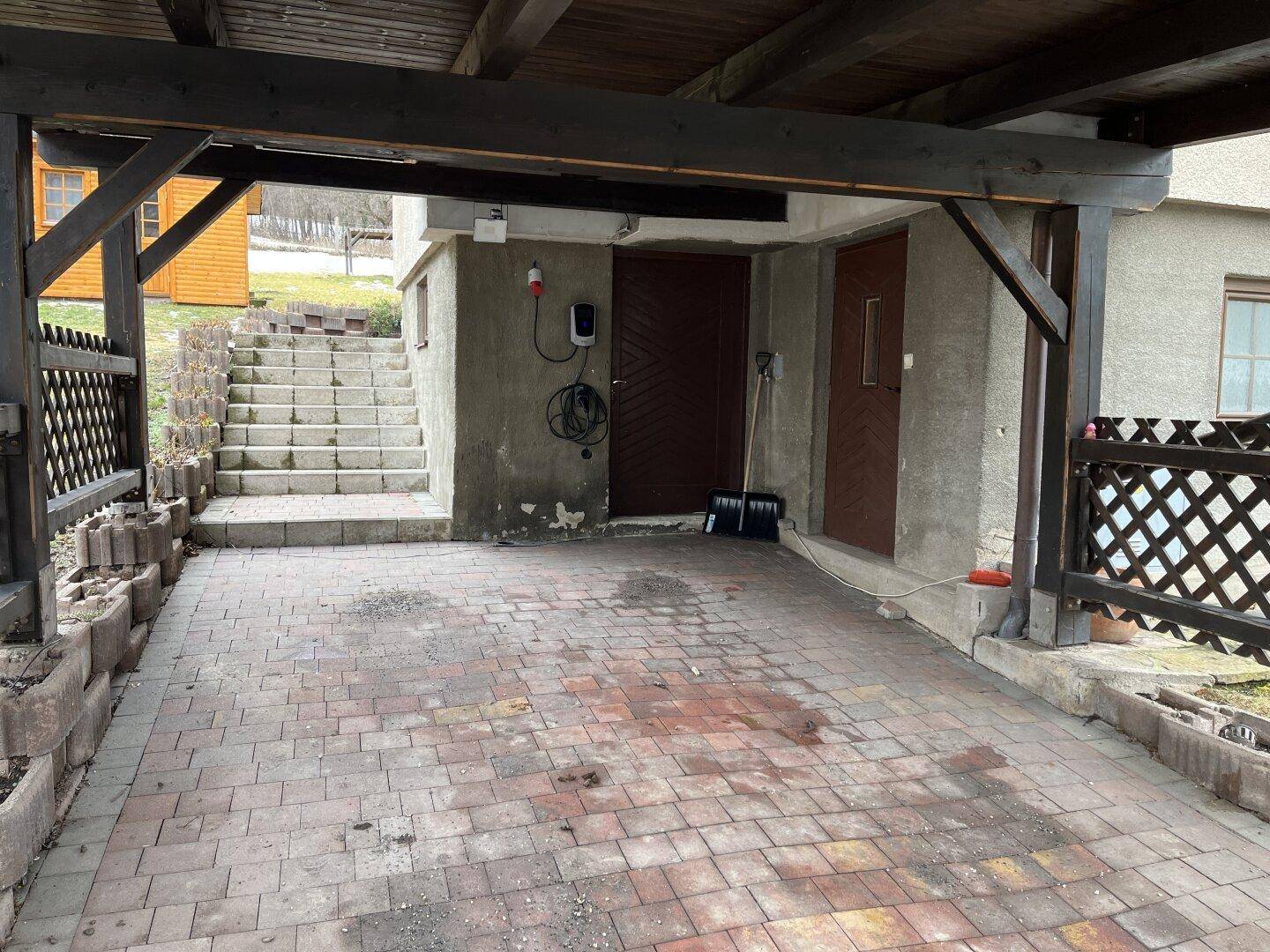 Überdachter Stellplatz (Carport) mit gepflastertem Boden und EV-Ladestation.