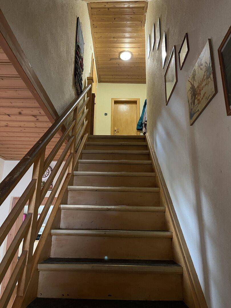 Holztreppe führt in den oberen Stock, mit Holzgeländer und Bildern an der Wand.