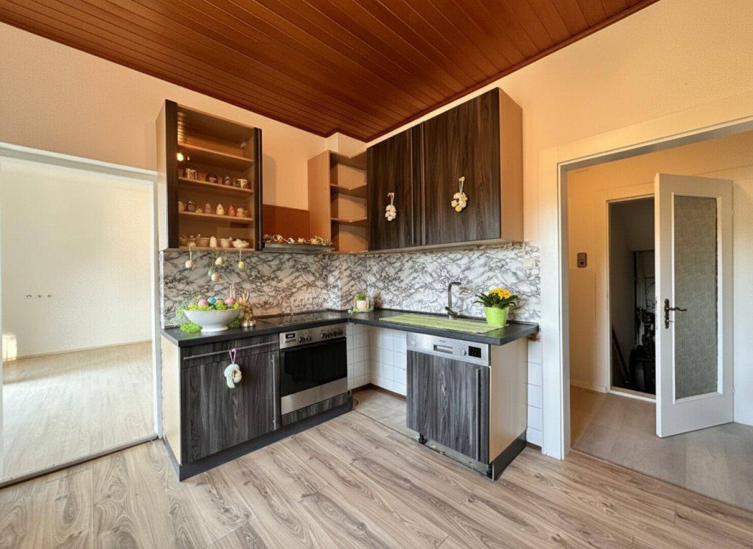 Funktionale Küche mit dunklen Holzfronten, Spülmaschine und Zugang zu angrenzenden Räumen.