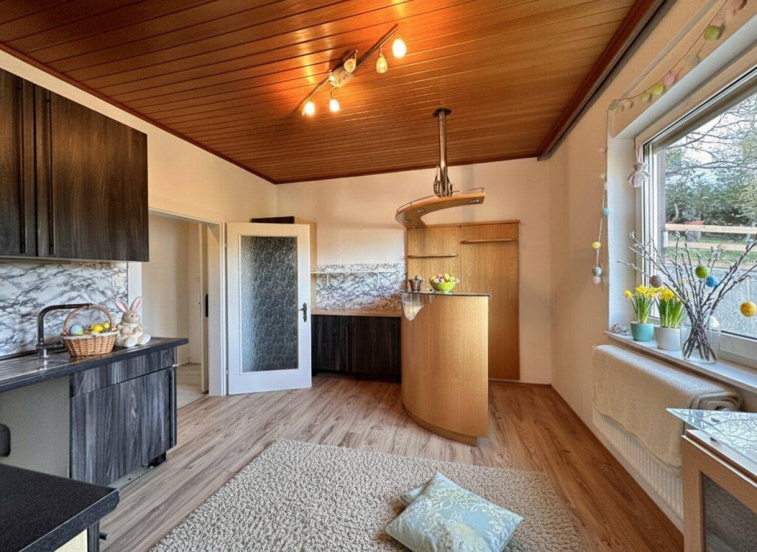 Helle Küche mit Holzdecke, funktionaler Bar und Zugang zu weiteren Räumen im Haus.