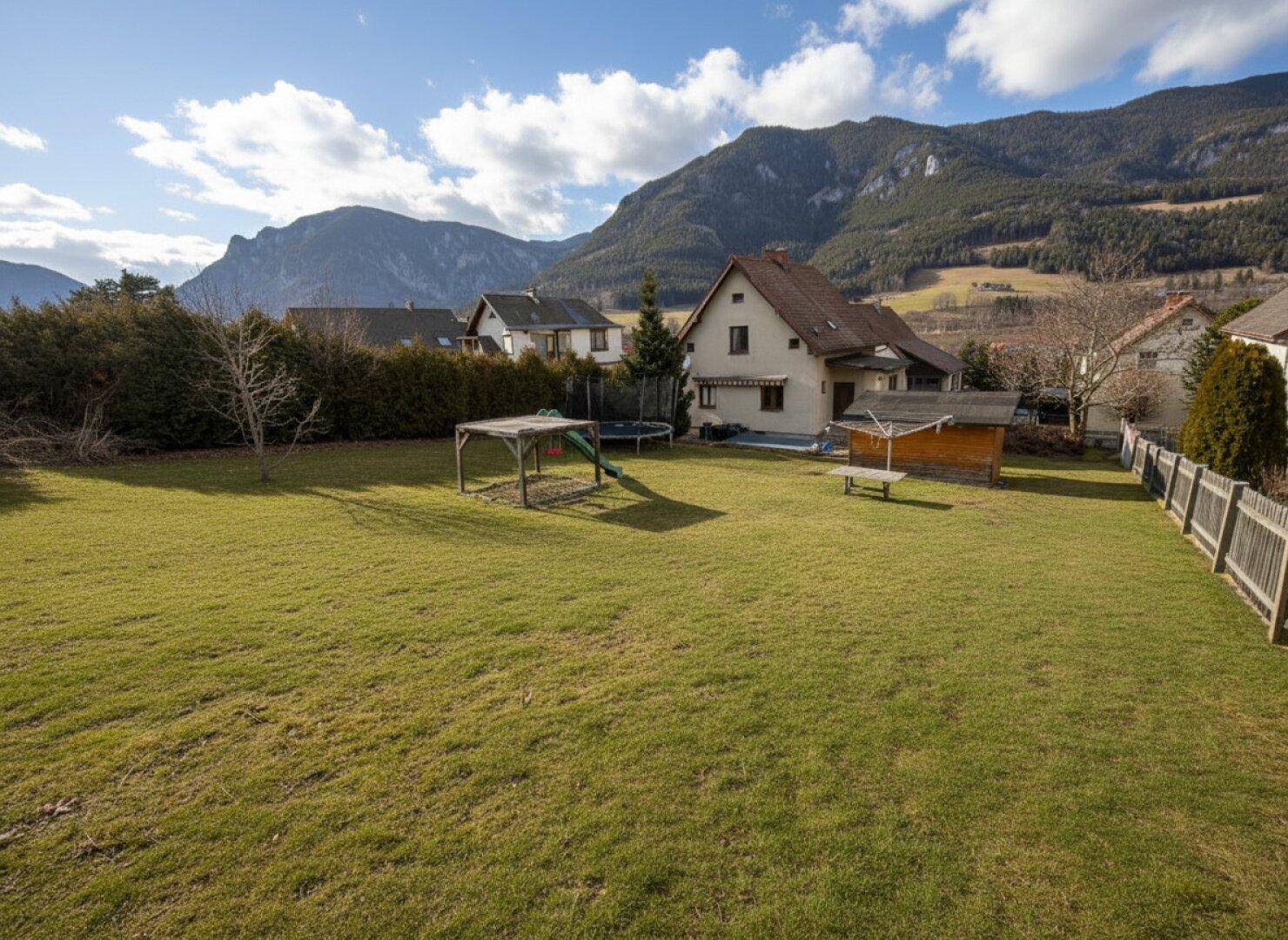 Großer Garten mit Rasenfläche, Spielgeräten und Blick auf die umliegenden Berge.
