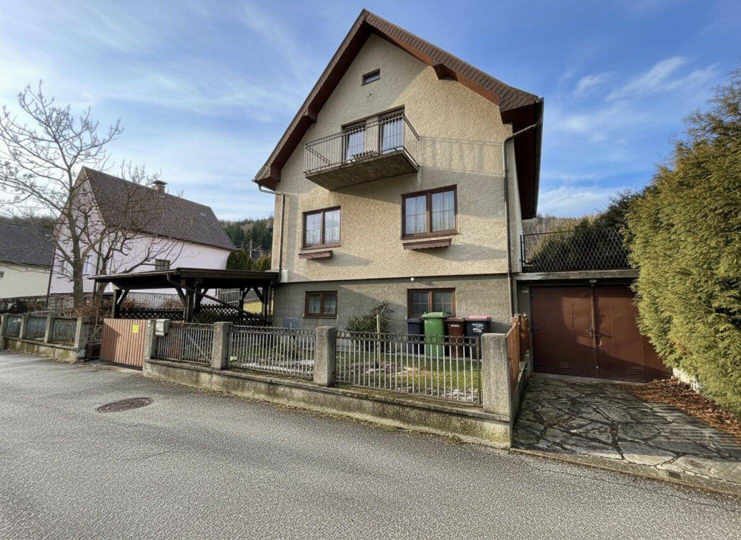 Einfamilienhaus mit Satteldach, Balkon und Garage an der Straße.