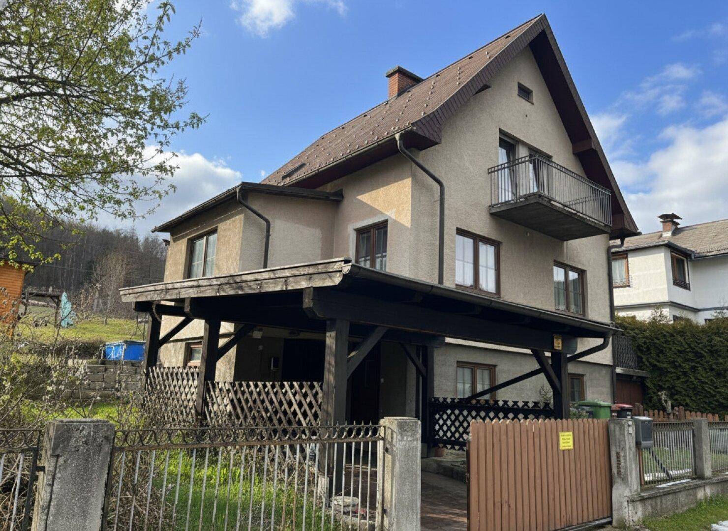 Einfamilienhaus mit Carport, Balkon und Satteldach in ländlicher Umgebung.