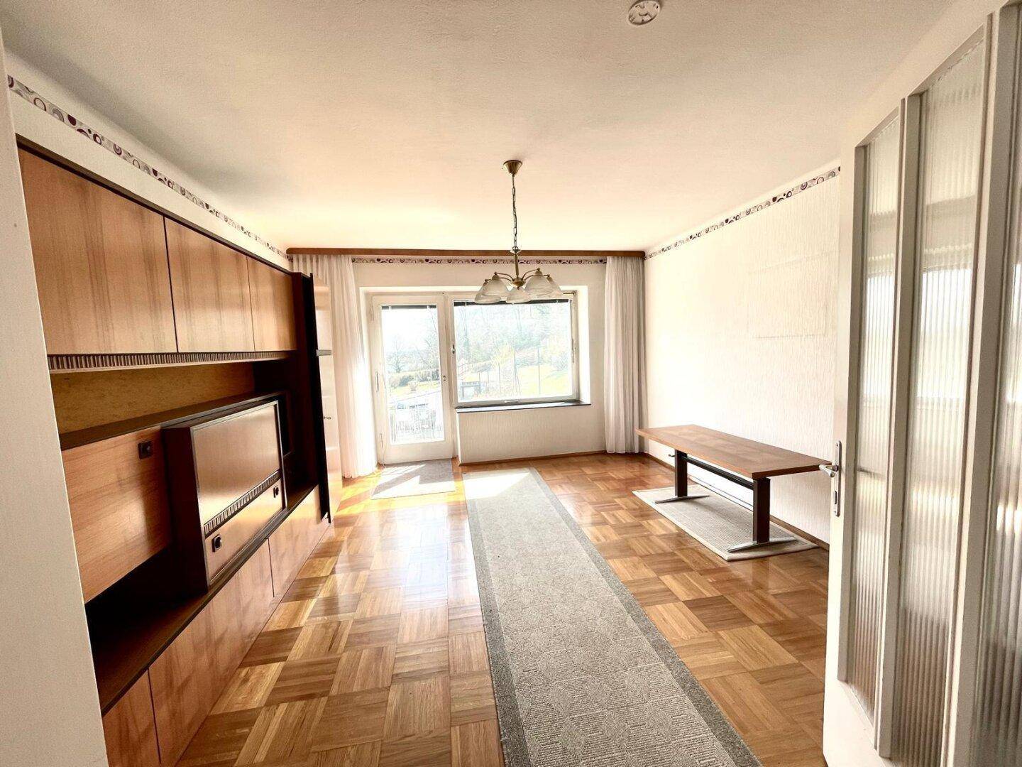 Helles Wohnzimmer mit Parkettboden, Einbauschrank und Zugang zum Balkon.