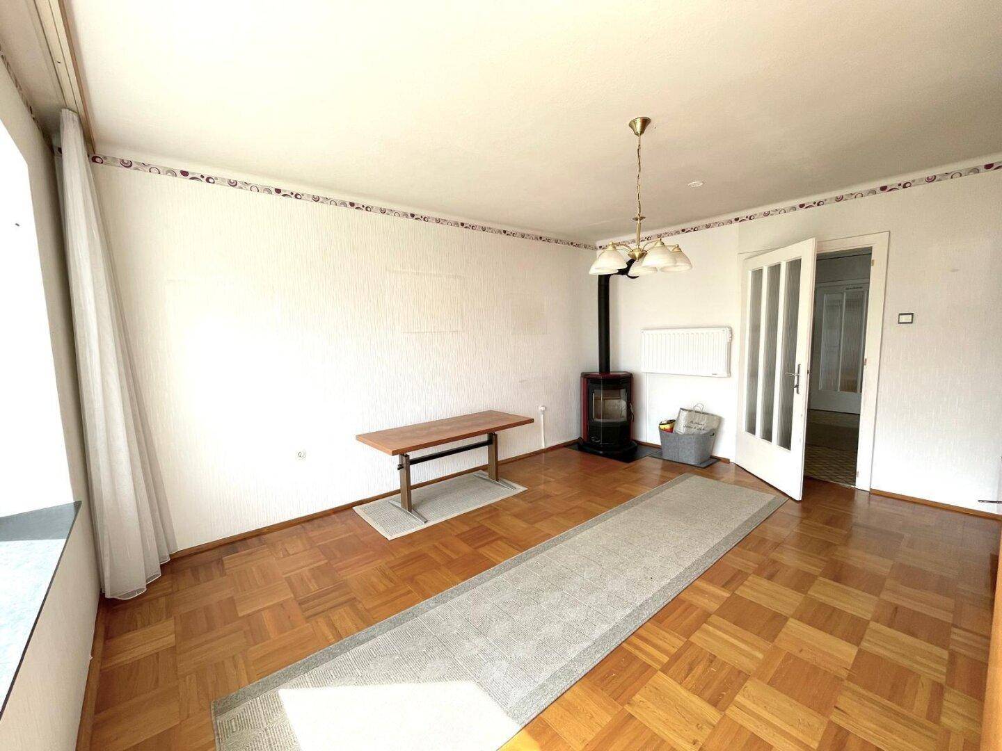 Geräumiges Wohnzimmer mit Parkettboden und einem Holzofen für gemütliche Abende.