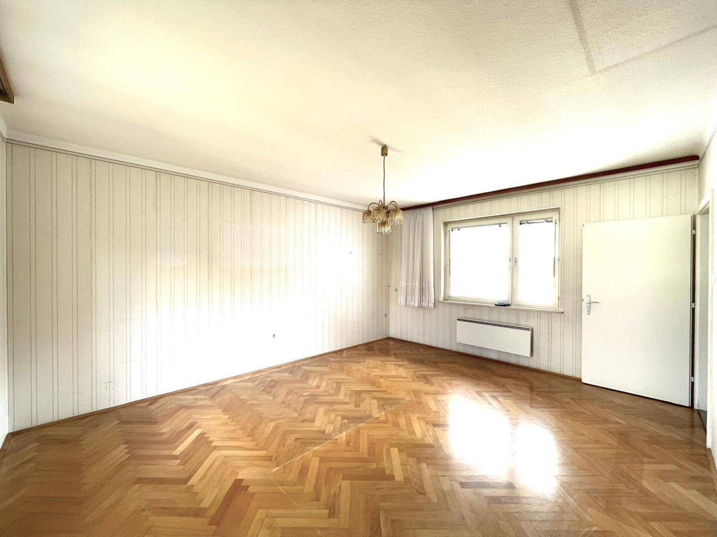 Helles Zimmer mit Parkettboden und schlichter Einrichtung.