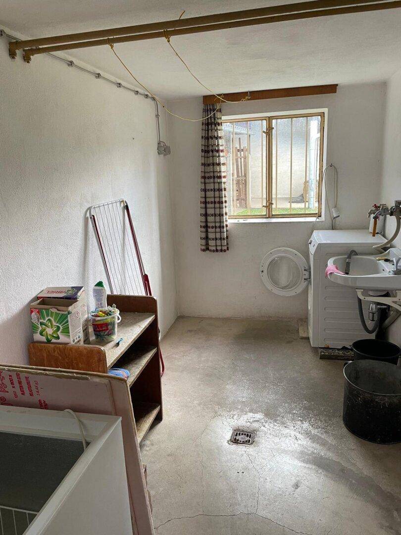 Waschküche im Keller mit Waschmaschine, Spülbecken und Fenster.