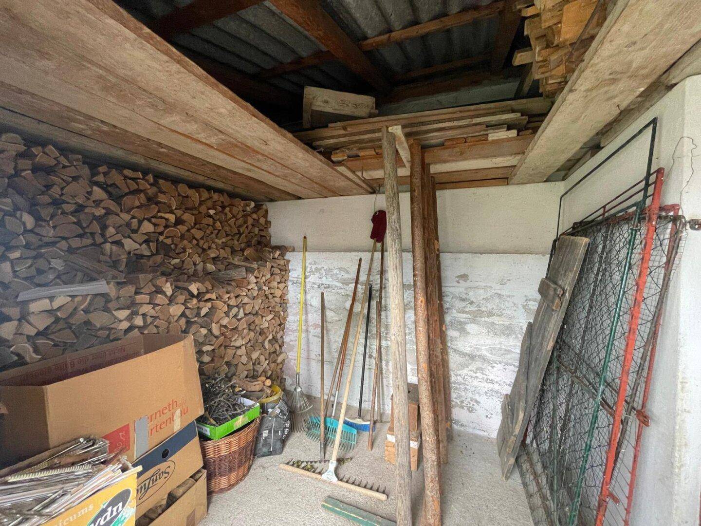 Lagerraum mit gestapeltem Brennholz und Holzregalen.