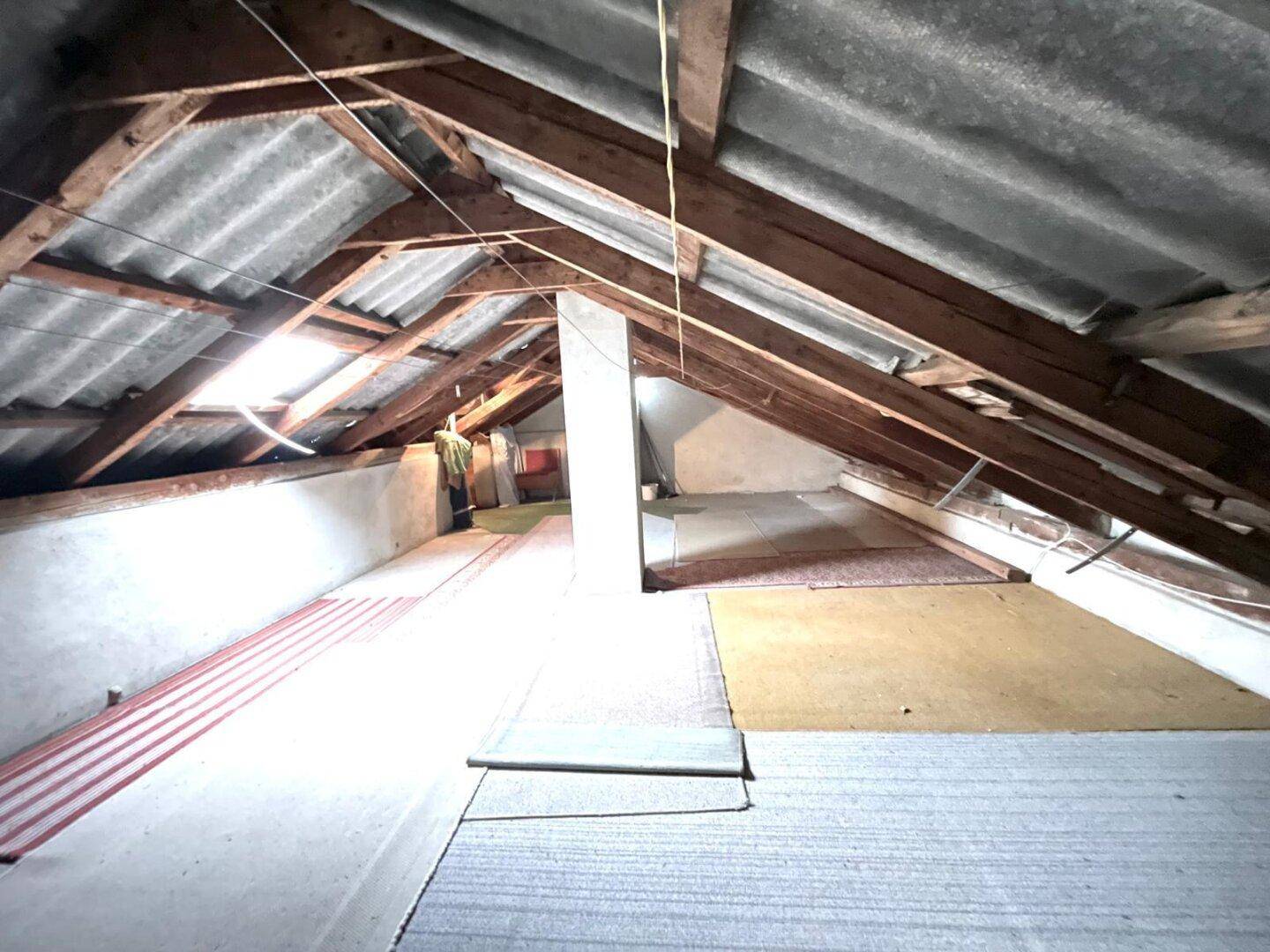 Dachboden mit sichtbaren Holzbalken und einfacher Dämmung.
