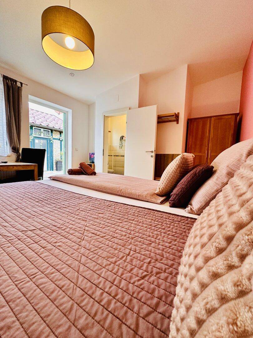 Nahaufnahme des Bettes in einem hellen Schlafzimmer mit Blick auf den Ausgang zum Hof.