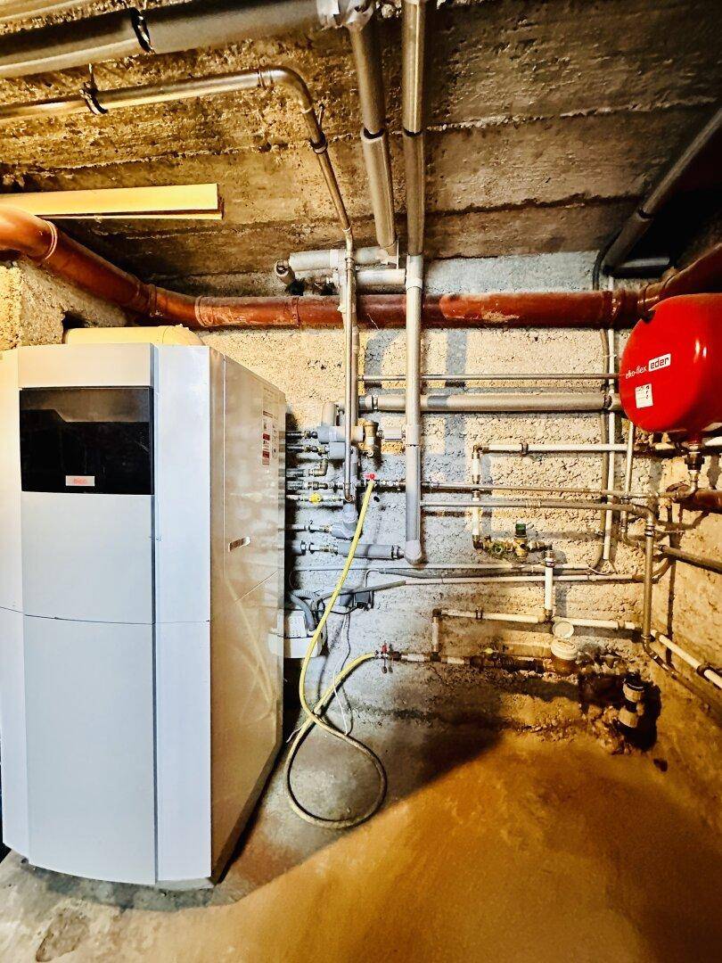 Heizungsraum im Keller mit moderner Heizungsanlage und sichtbaren Rohrleitungen.