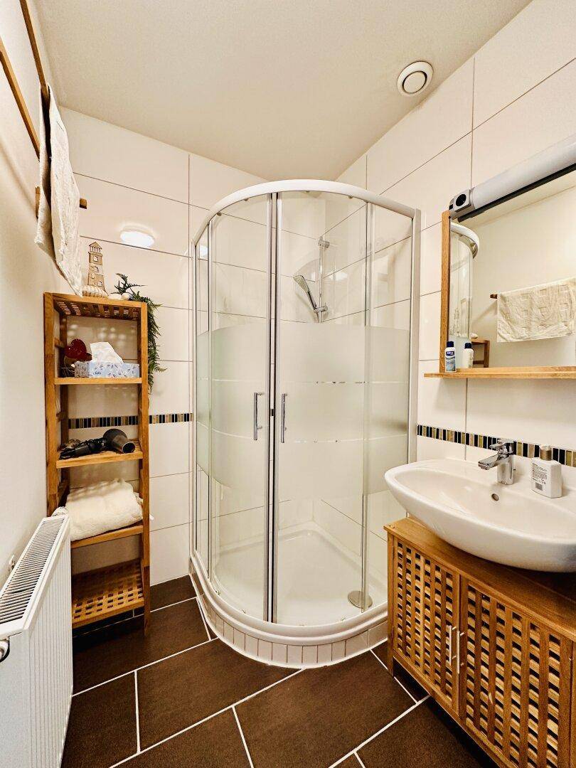 Helles Badezimmer mit Eckduschkabine, Waschbecken und praktischen Holzregalen.
