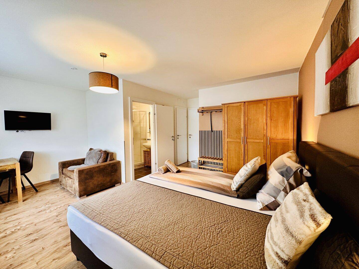 Geräumiges Schlafzimmer mit Doppelbett, Sessel, Kleiderschrank und Badezimmerzugang.