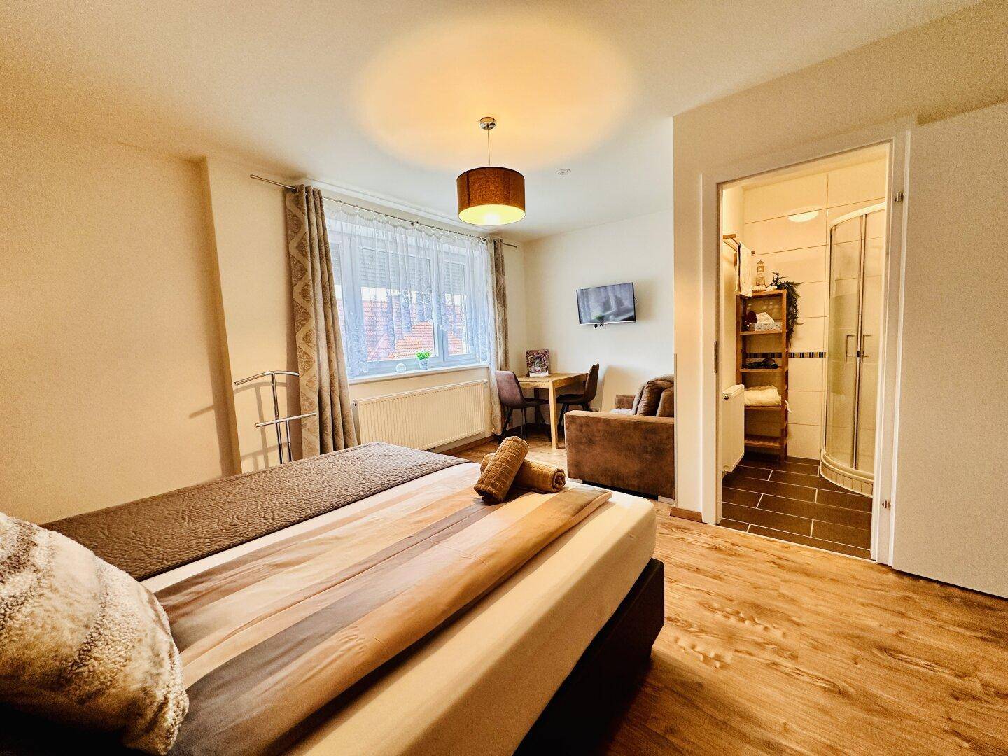 Gemütliches Schlafzimmer mit Bett, Sessel, kleinem Tisch und Zugang zum Duschbad.