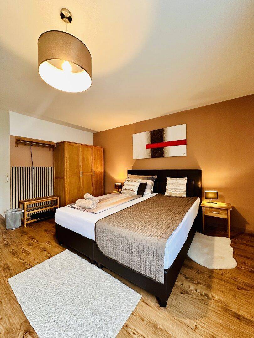 Schlafzimmer mit Doppelbett, Holzschrank und einem modernen Gemälde an der braunen Wand.