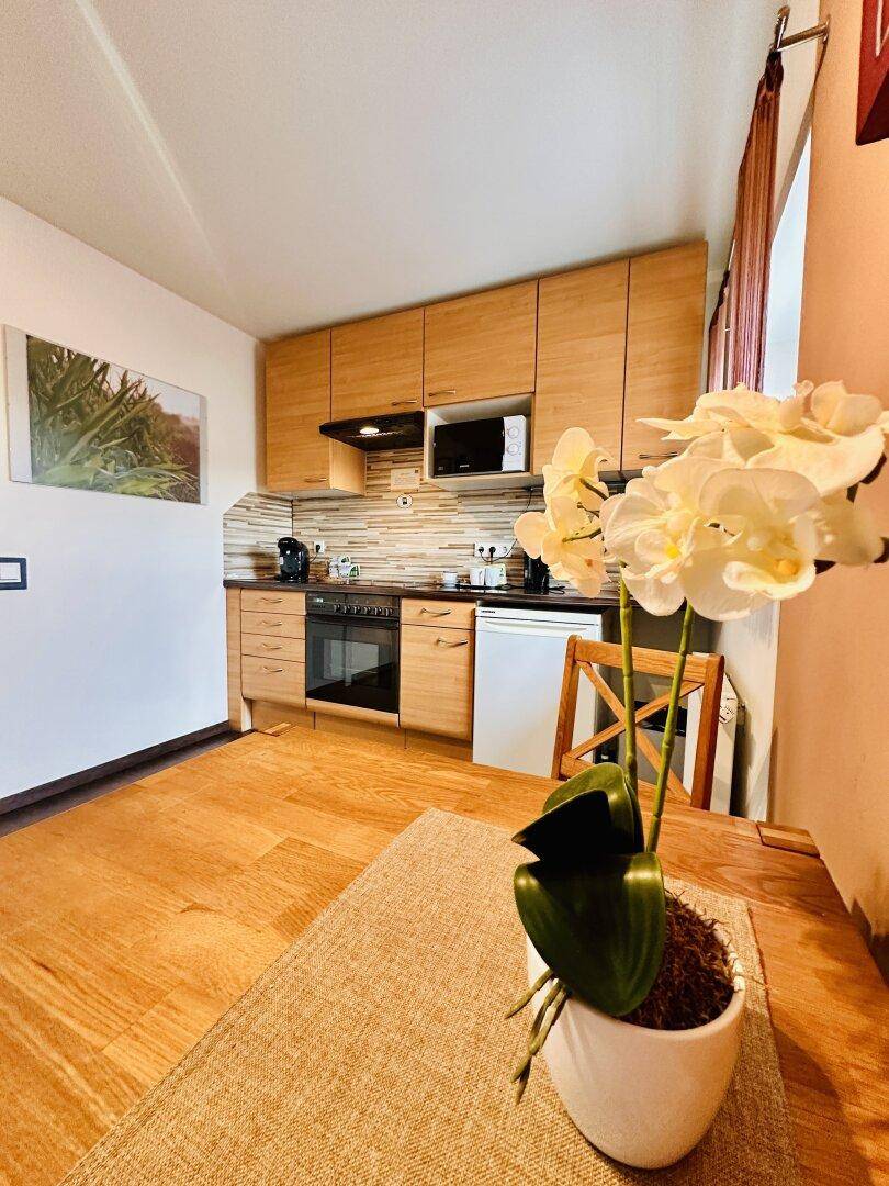 Moderne Küche mit hellen Holzfronten, Essbereich und Blick auf eine Orchidee.