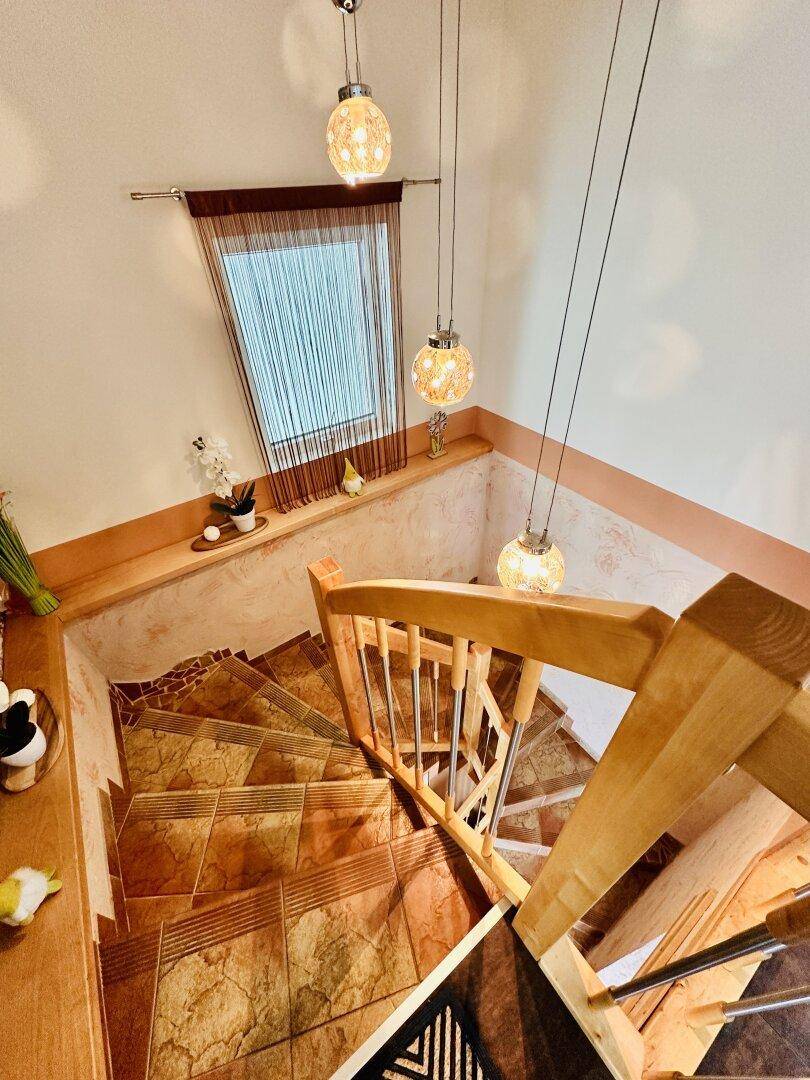 Wendeltreppe mit gefliesten Stufen und Holzgeländer, von oben fotografiert.