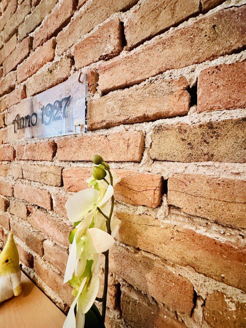 Detailaufnahme einer Ziegelwand mit einem Schild "Anno 1927" und einer Orchideenpflanze.
