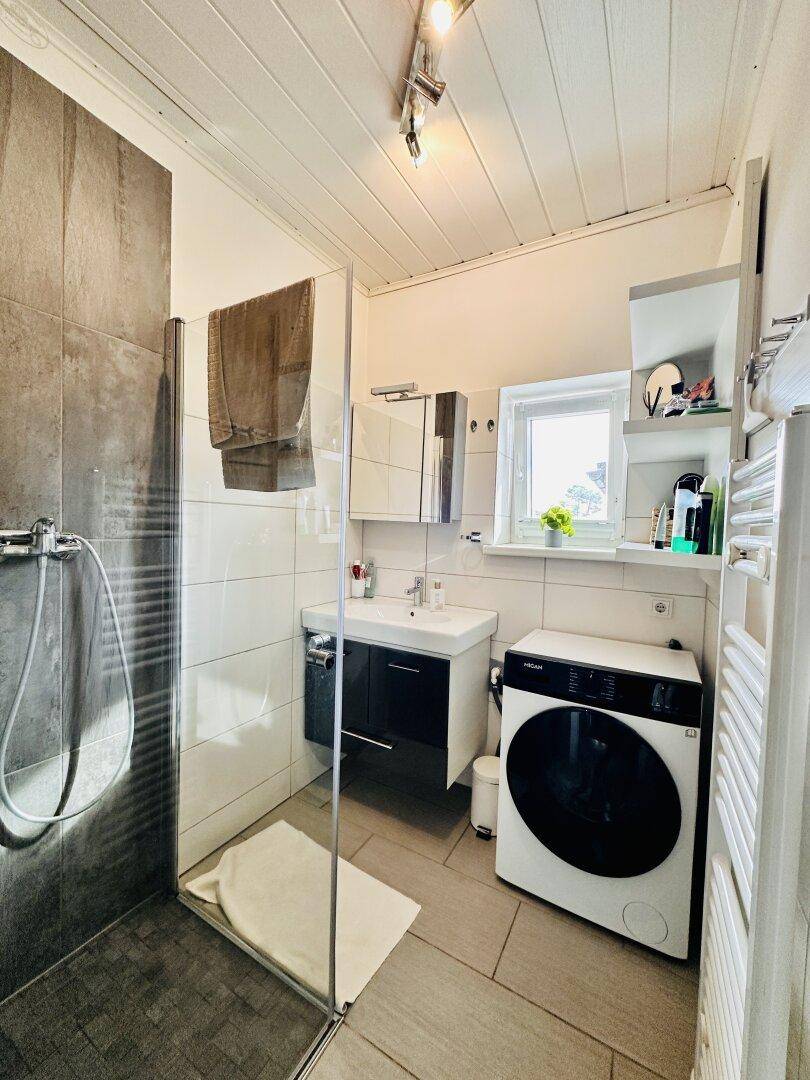 Modernes Badezimmer mit begehbarer Dusche, Waschbecken, Waschmaschine und Fenster.