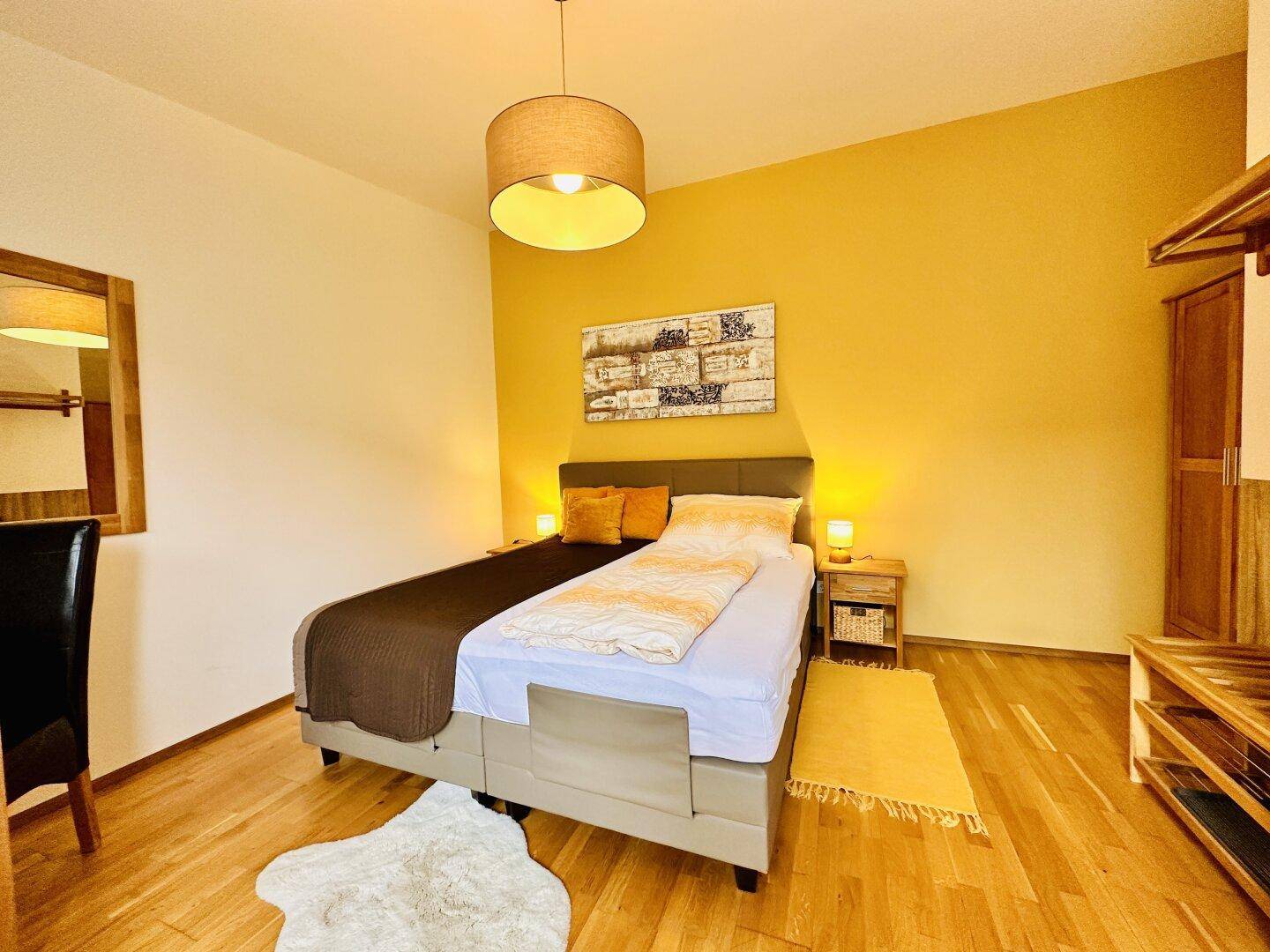 Helles Schlafzimmer mit Doppelbett, Nachttischen und einem Spiegel an der Wand.