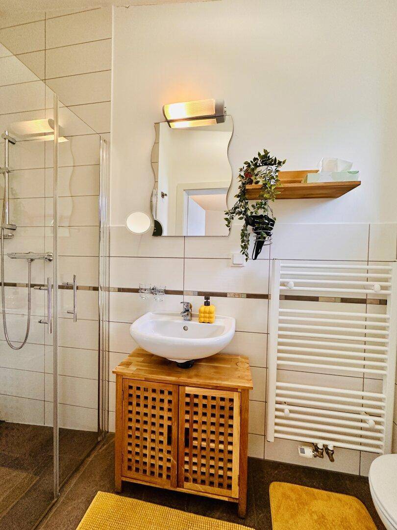 Modernes Badezimmer mit Waschbecken, Spiegel, Duschbereich und beheiztem Handtuchhalter.