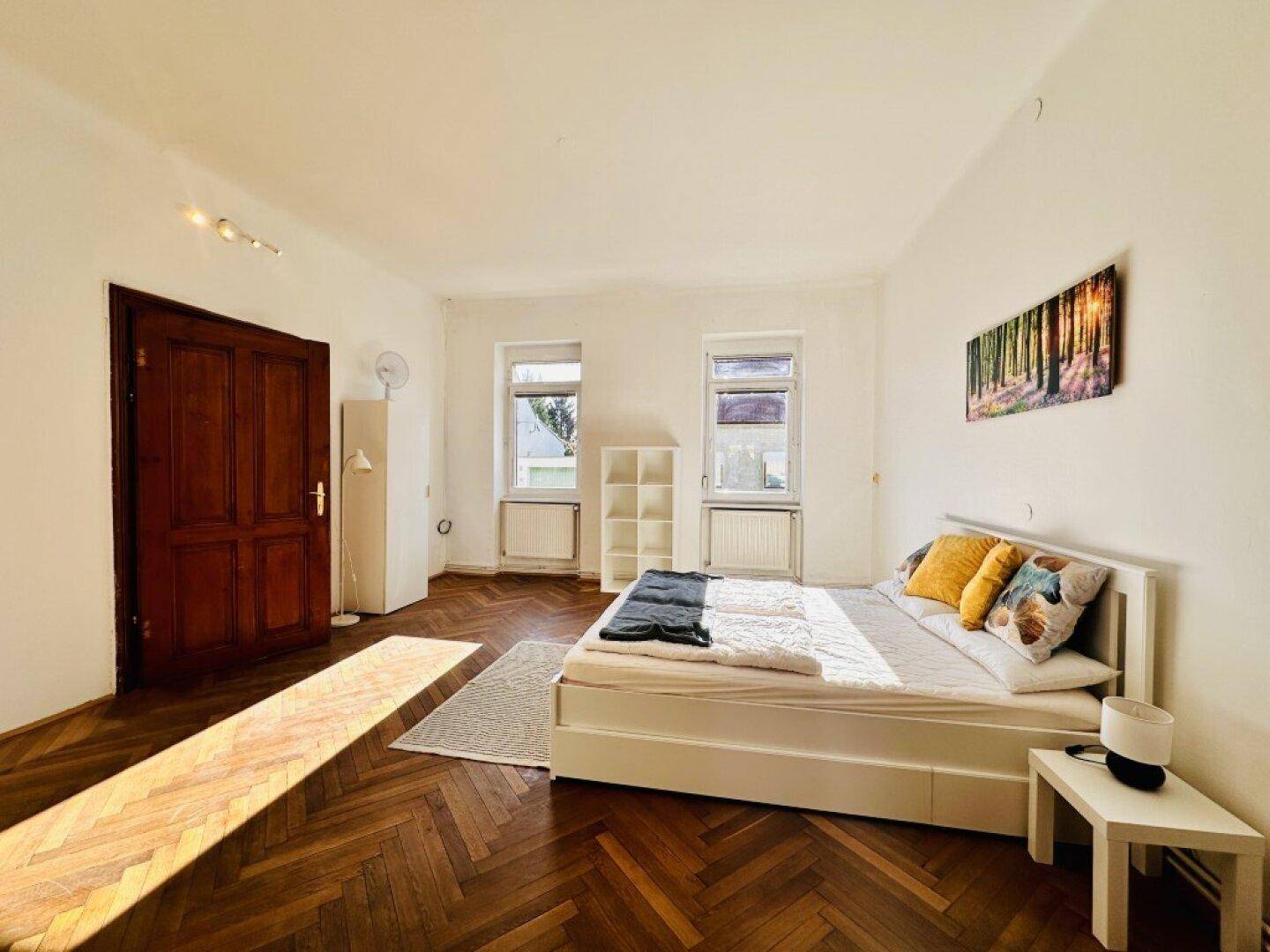 Geräumiges Schlafzimmer mit Fischgrätparkett, einem Doppelbett und viel Tageslicht.