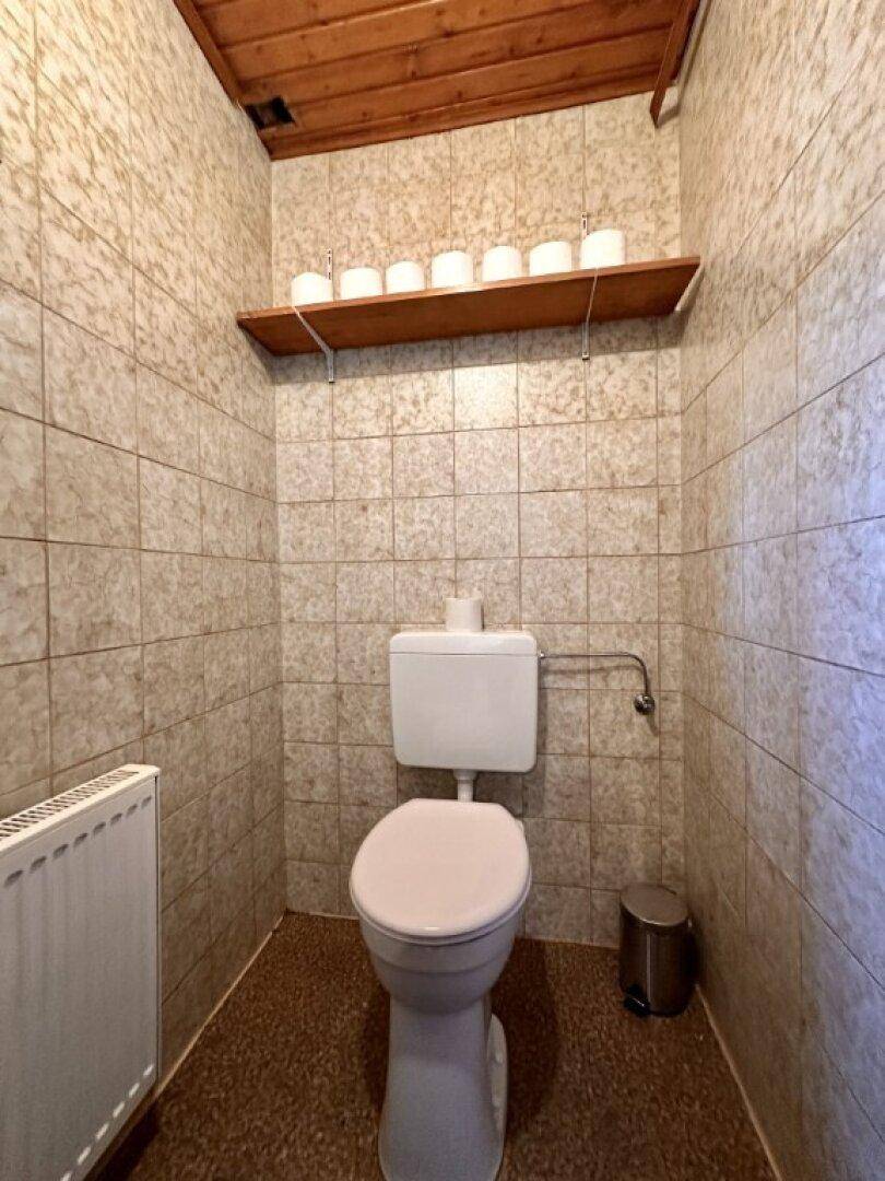Separate Toilette mit WC, Fliesen und einer Holzdecke.