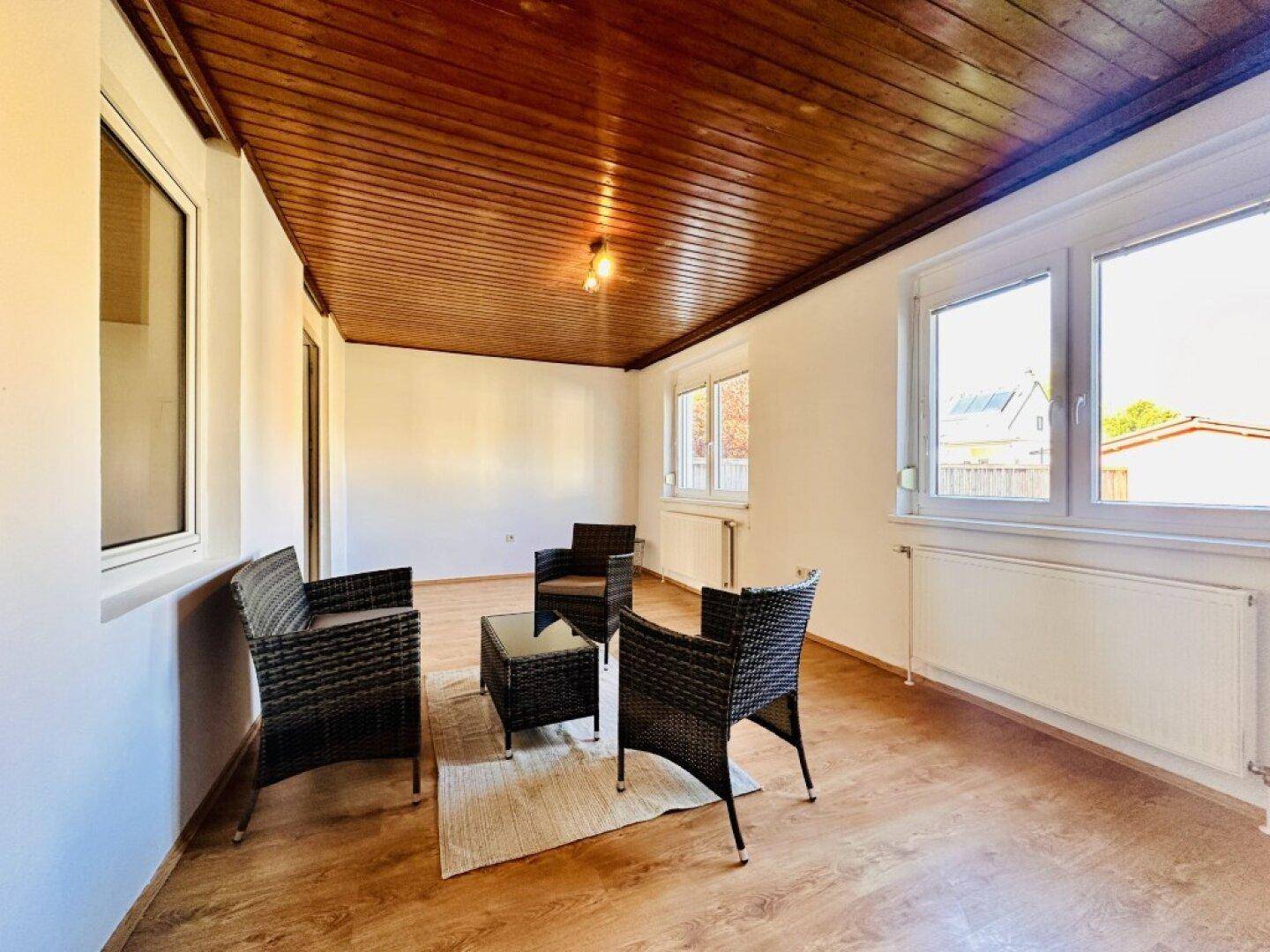 Heller Raum mit Holzdecke, Laminatboden und vier Korbsesseln.