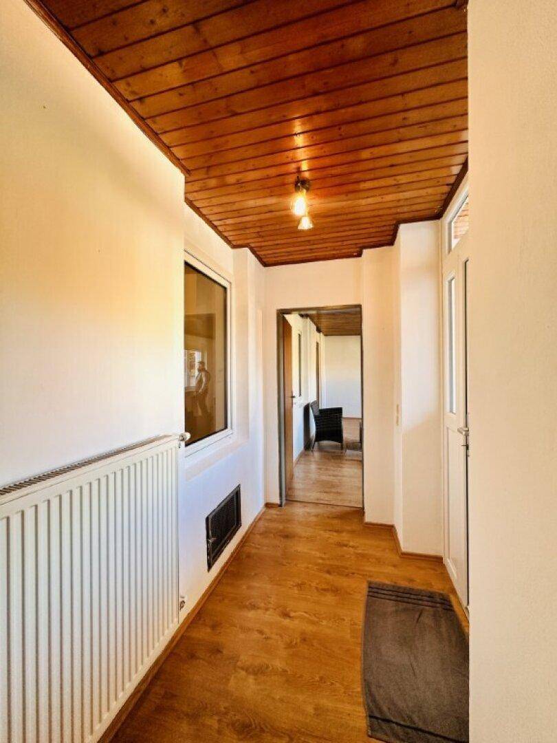 Flur mit Holzdecke, Laminatboden und einem Heizkörper unter dem Fenster.