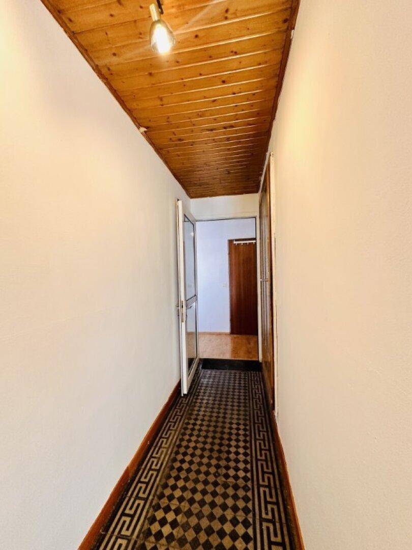 Langer Flur mit kariertem Fliesenboden und einer Holzdecke.