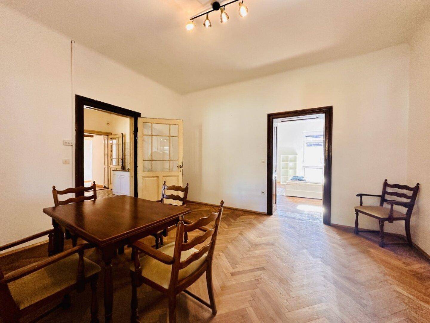 Esszimmer mit Holztisch und Stühlen, Fischgrätparkett und Zugang zu weiteren Räumen.