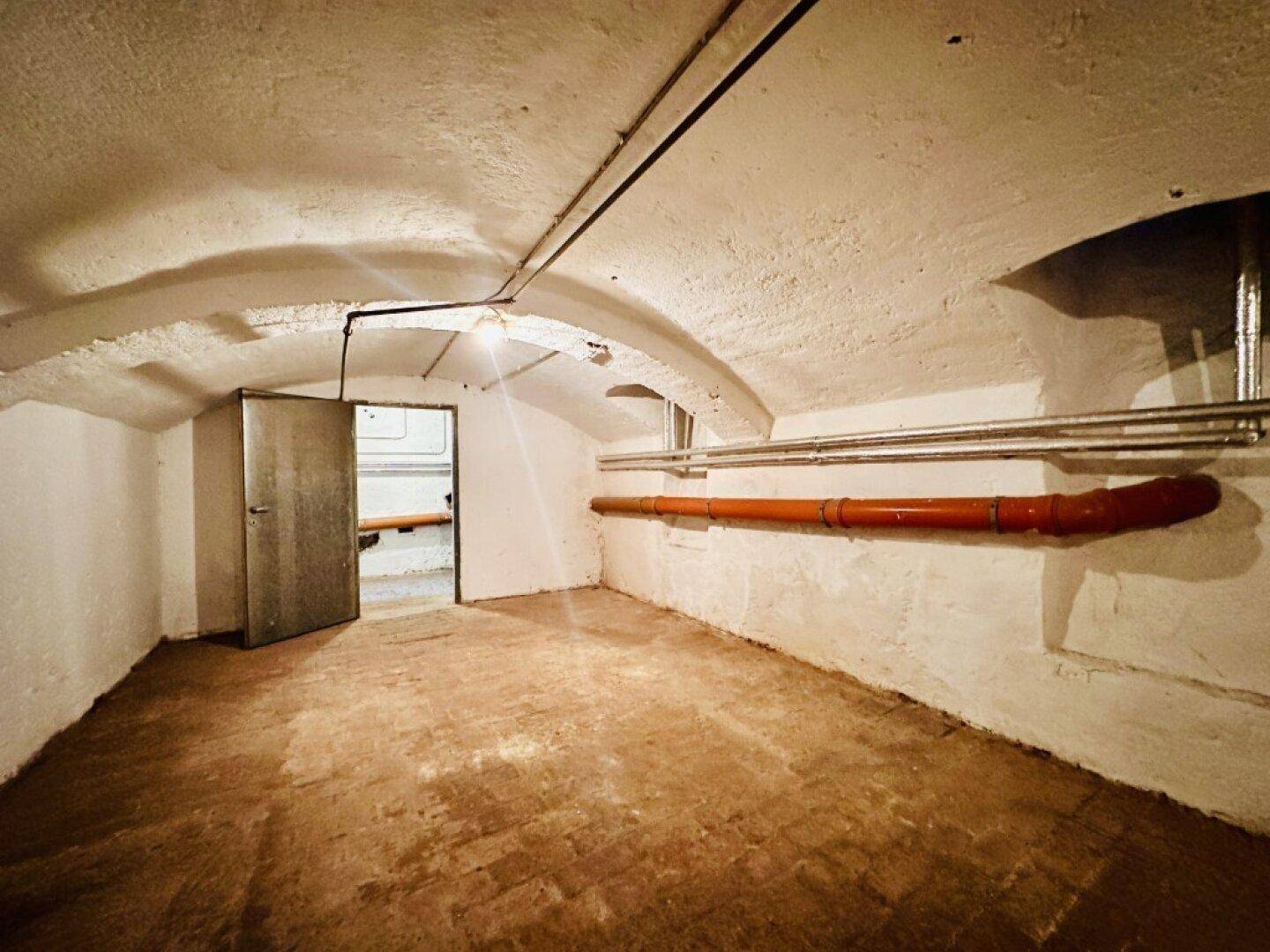 Geräumiger Kellerraum mit gewölbter Decke, unverputzten Wänden und sichtbaren Rohren.