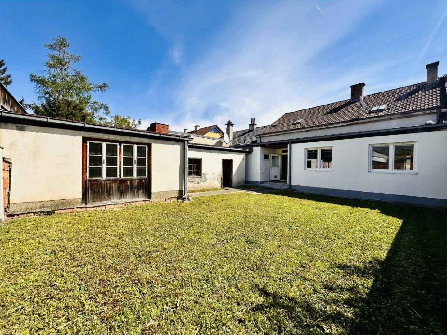 Hinterhof mit großem Rasen und mehreren Nebengebäuden unter blauem Himmel.