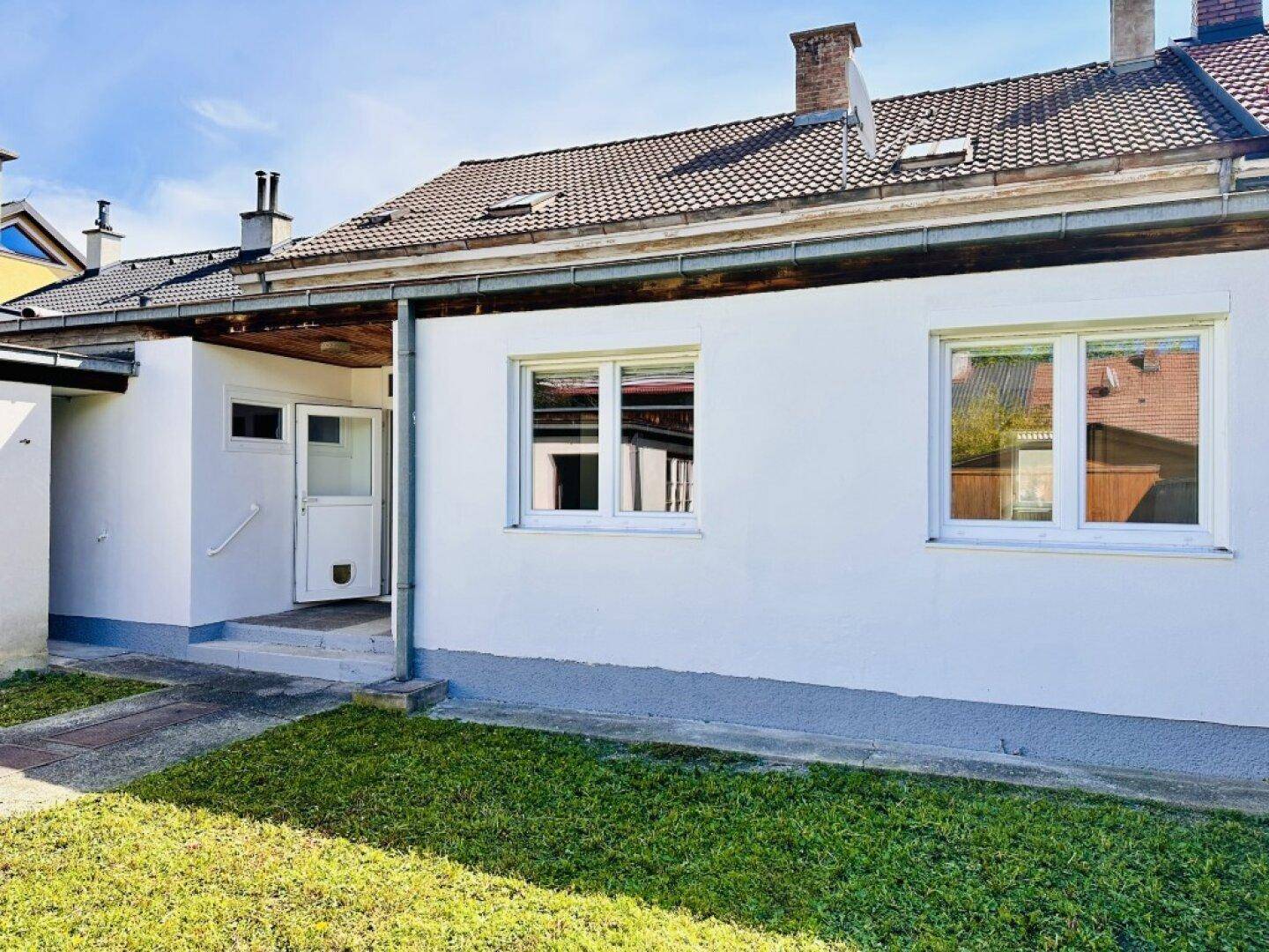 Einfaches Einfamilienhaus mit weißer Fassade, braunem Ziegeldach und kleinem Vorgarten.
