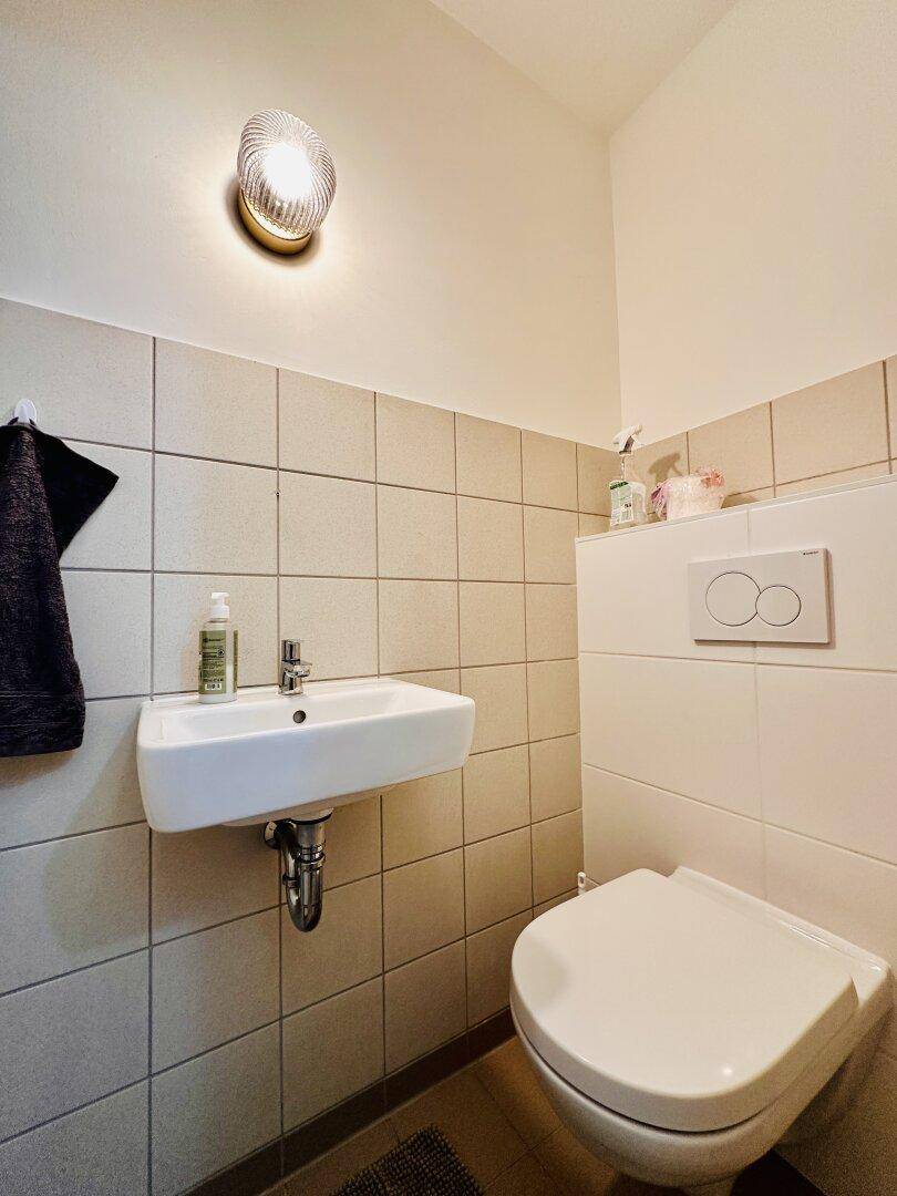 Modernes Gäste-WC mit Wand-WC und kleinem Waschbecken, halbhoch gefliest.