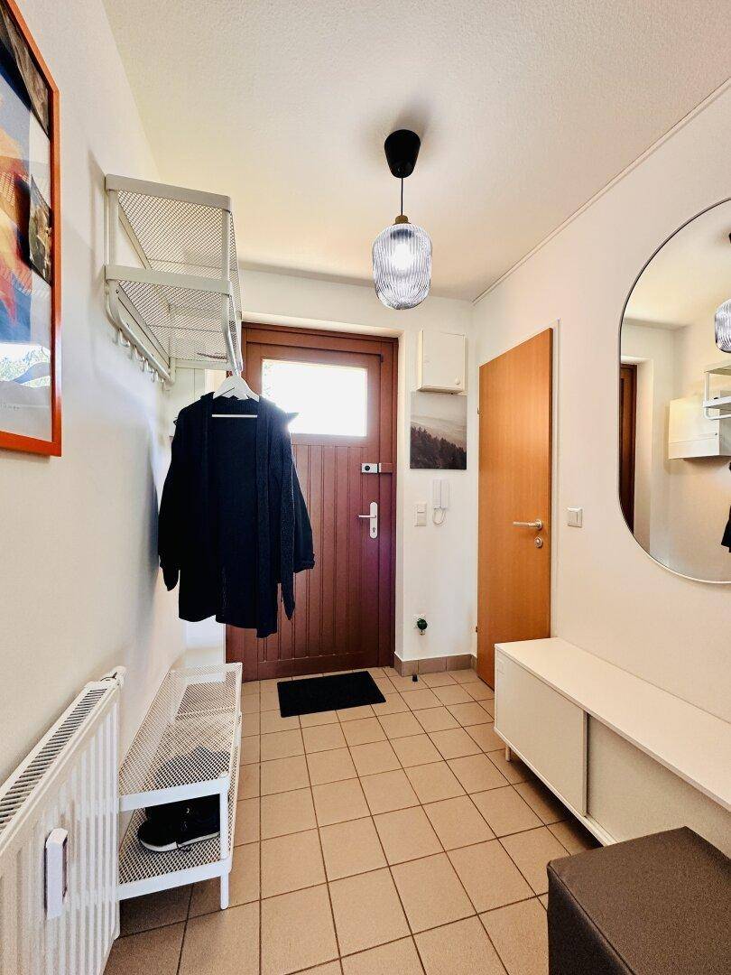 Eingangsbereich mit Fliesenboden, Garderobe und Spiegel, hell und einladend gestaltet.