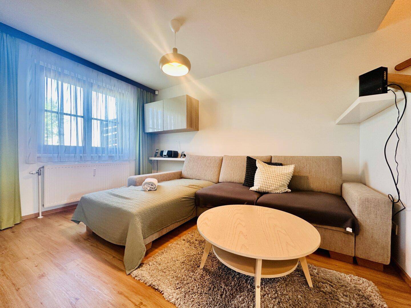 Gemütliches Wohnzimmer mit beigem Sofa, Couchtisch und Holzboden, hell durch große Fenster.
