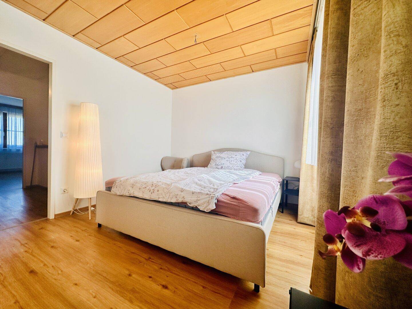 Gemütliches Schlafzimmer mit Holzboden, Holztäfelung an der Decke und großem Bett.