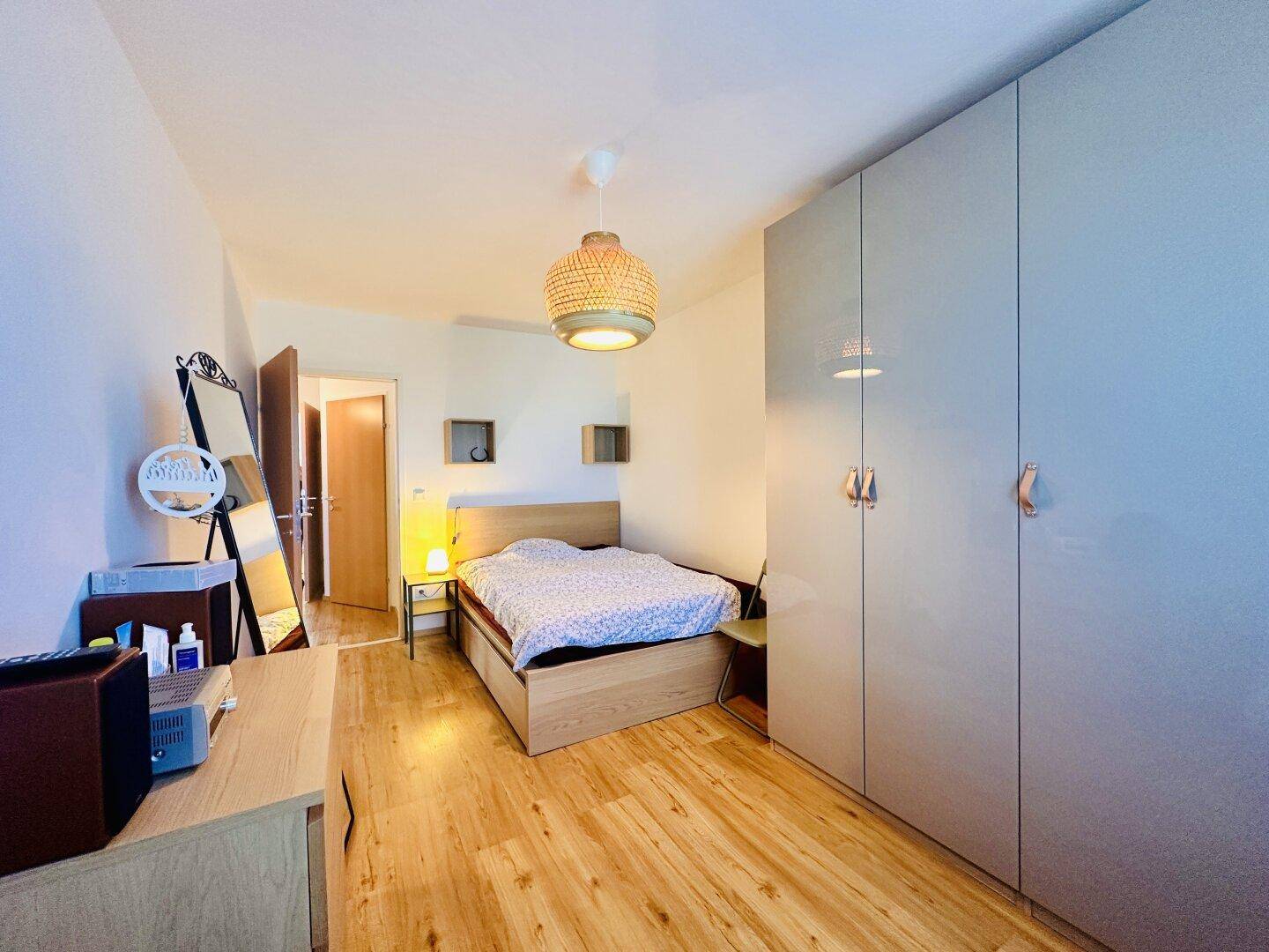 Helles Schlafzimmer mit Holzboden, modernem Bett und großem grauen Kleiderschrank.