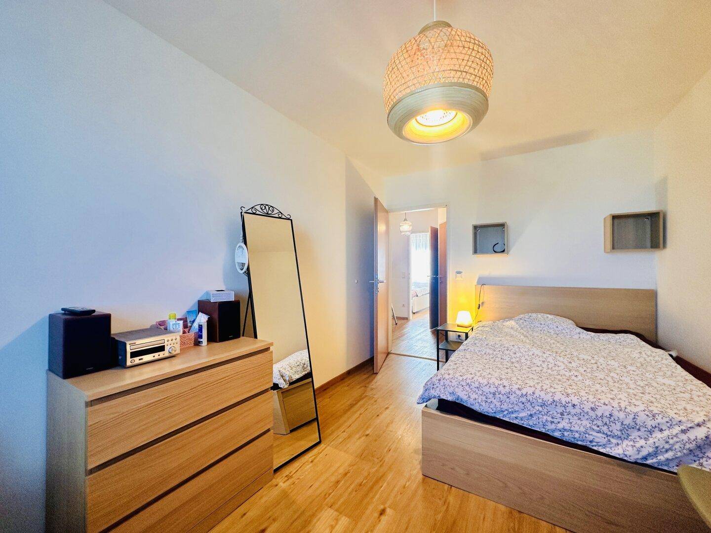 Schlafzimmer mit Holzboden, Kommode und Spiegel, hell und funktional eingerichtet.