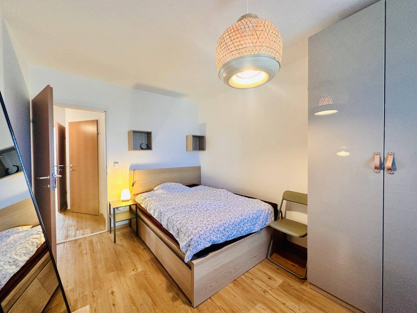 Helles Schlafzimmer mit Holzboden, modernem Bett und großem grauen Kleiderschrank.
