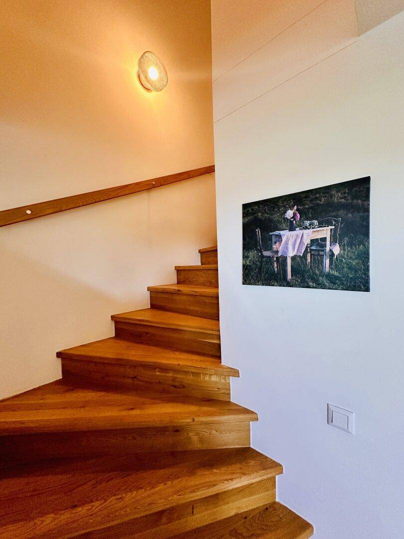 Holztreppe mit hellem Geländer, die in die obere Etage führt, mit Wanddekoration.