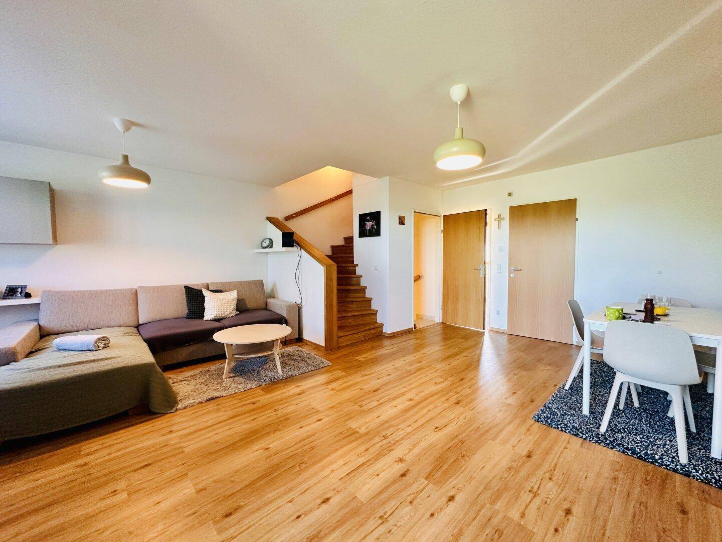 Offener Wohn- und Essbereich mit Holzboden und Treppe, die in die obere Etage führt.