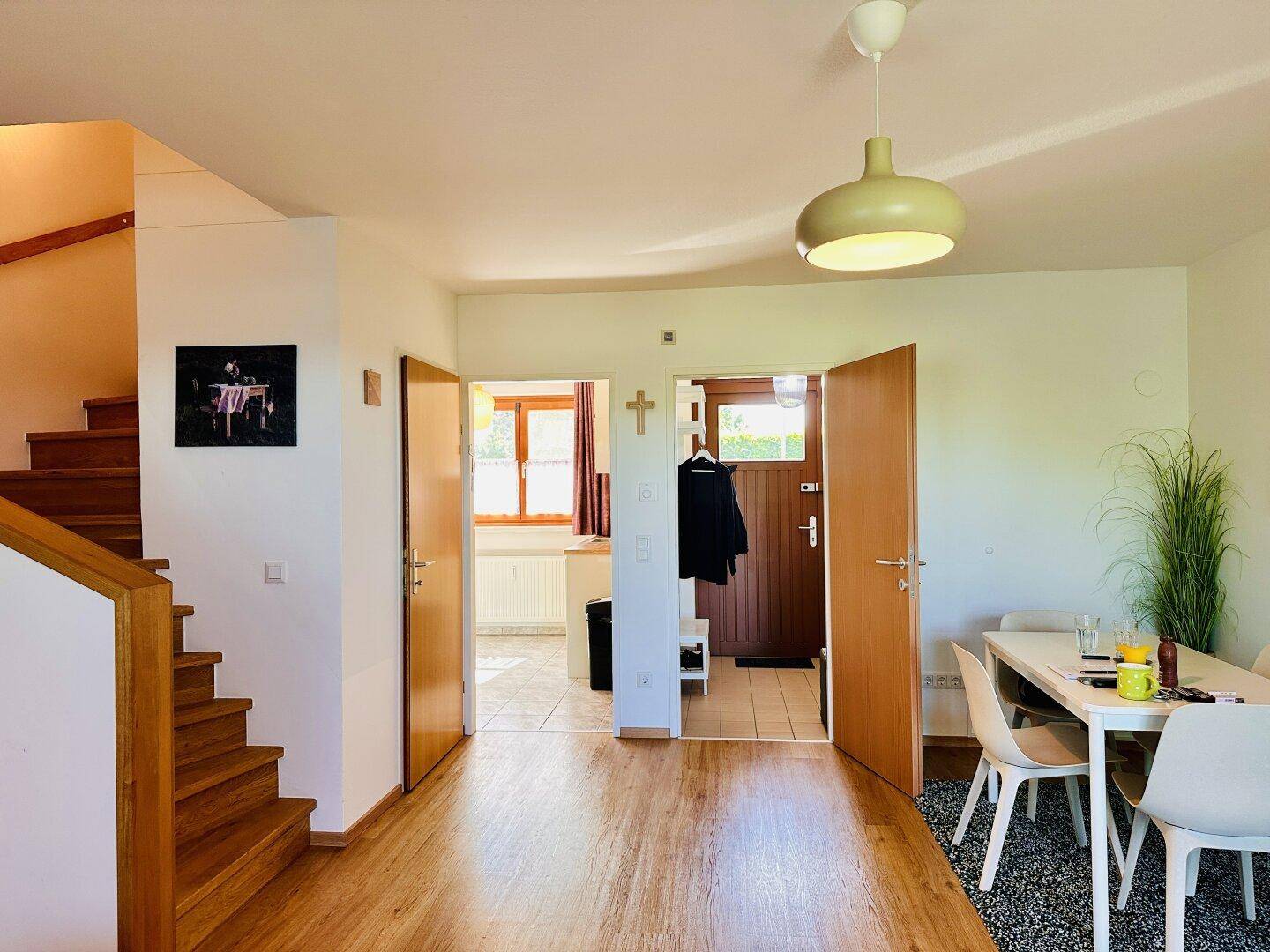 Heller Essbereich mit Holzboden und Blick auf die Küche, verbunden durch einen offenen Flur.