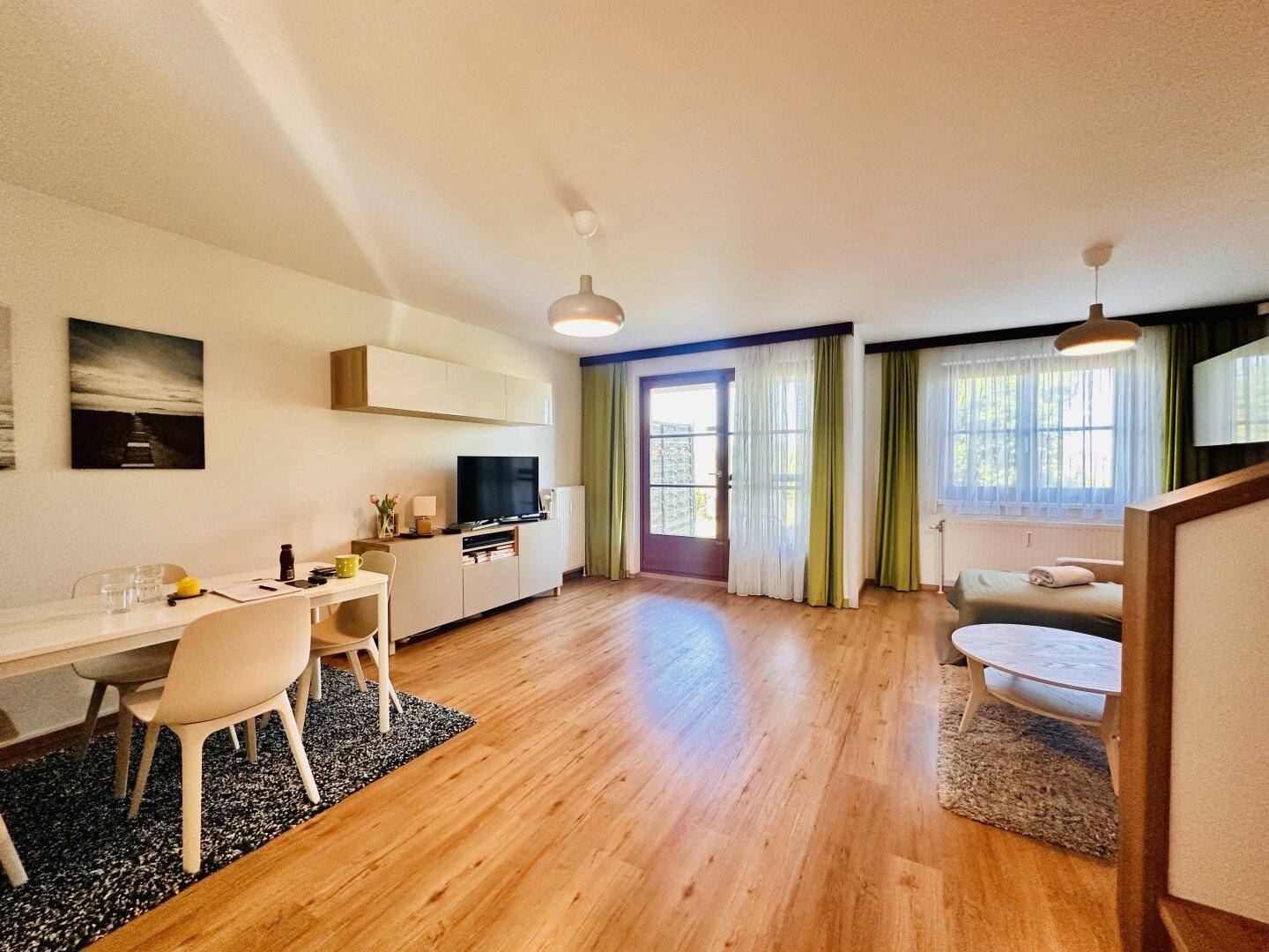 Geräumiger Wohn- und Essbereich mit Holzboden und Zugang zu einem Balkon oder einer Terrasse.