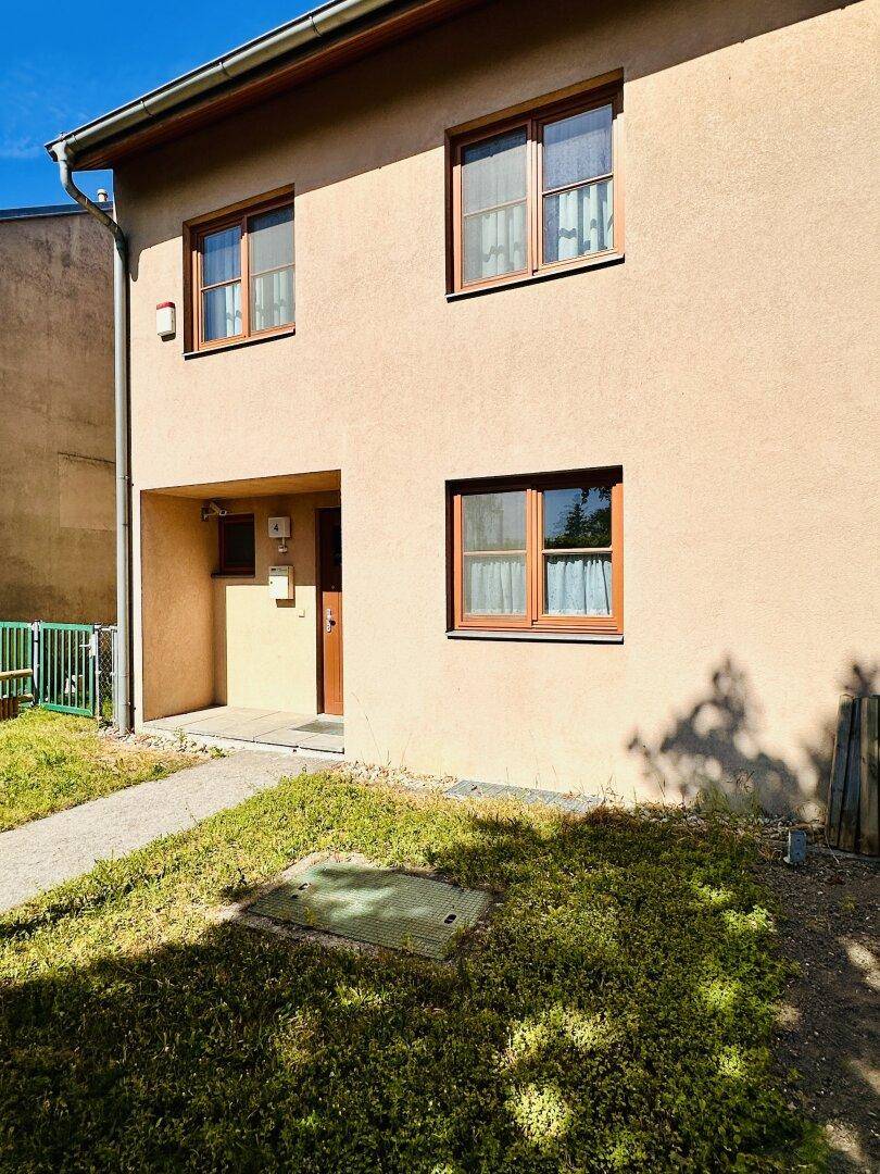 Vorderansicht des Hauses mit Eingangsbereich, kleinen Fenstern und gepflegtem Vorgarten.