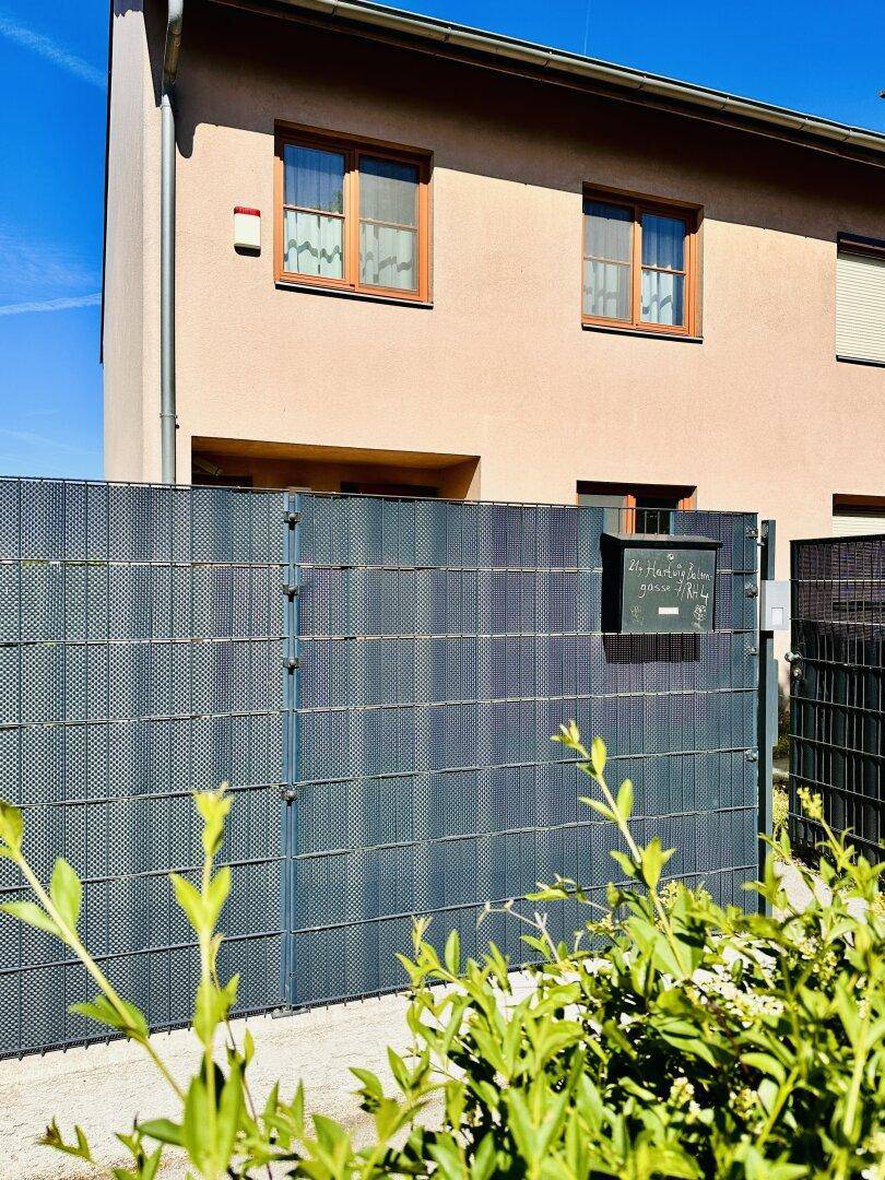 Hausfassade hinter einem modernen Zaun mit Briefkasten, bei sonnigem Wetter.