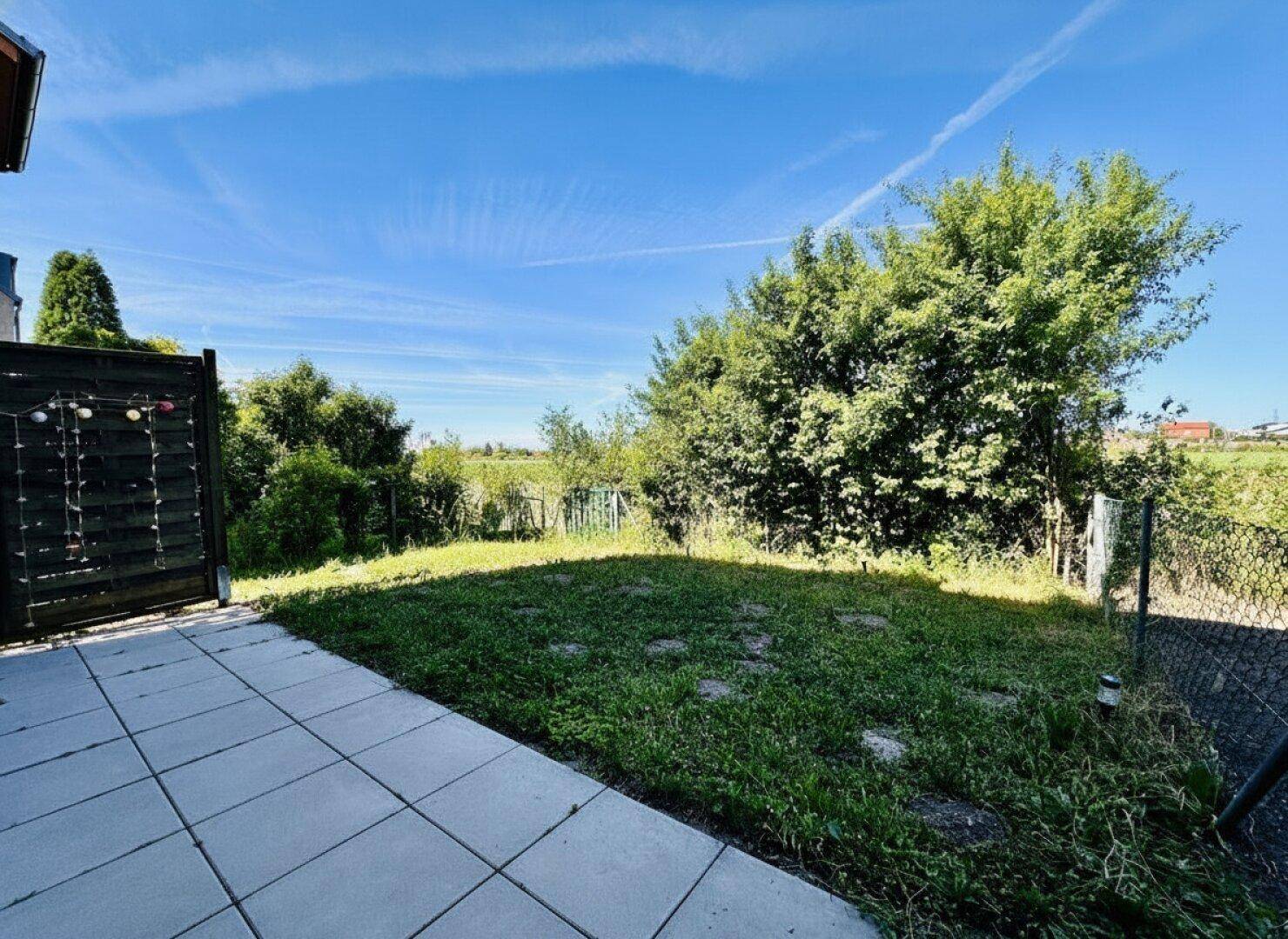 Blick von der Terrasse auf einen grünen Gartenbereich mit weitem Blick ins Grüne und offene Landschaft.